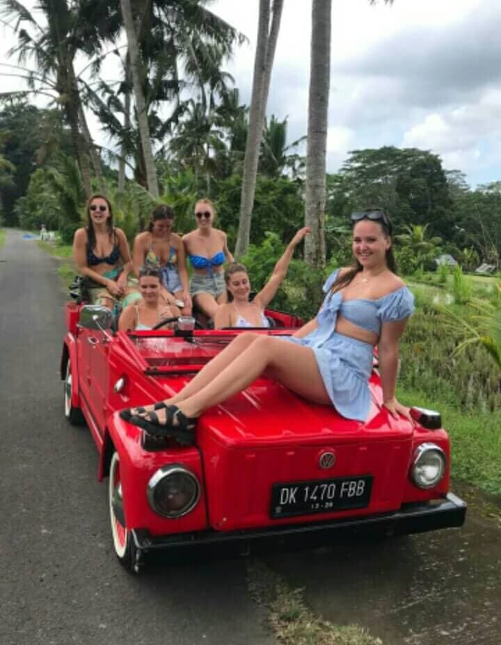 A birthday group posing beside the car at a jungle waterfall stop.